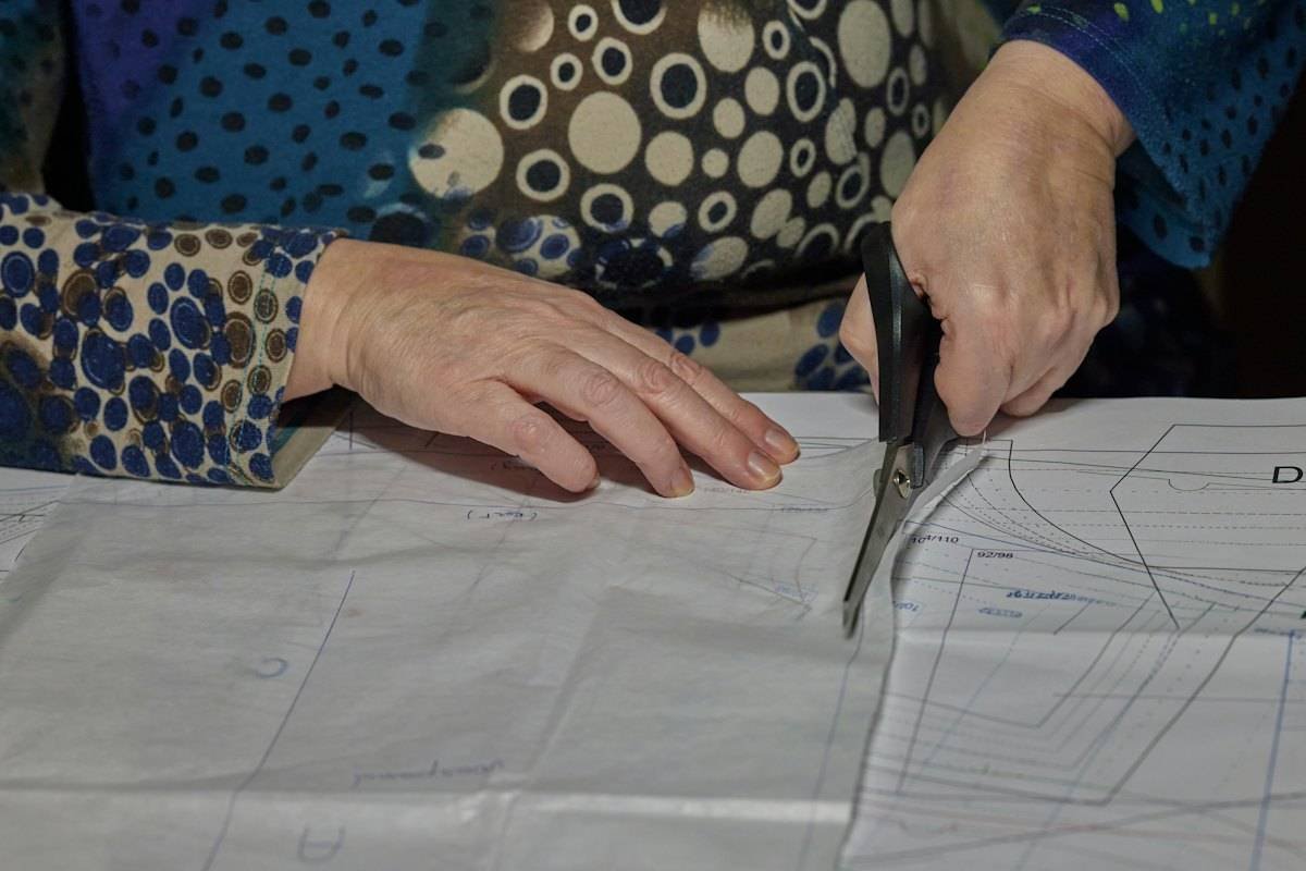 Hands cutting a paper sewing pattern with tailoring shears